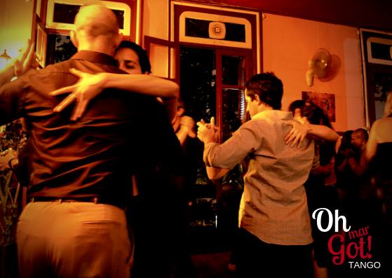 Parejas bailando tango en un salón, a media luz
